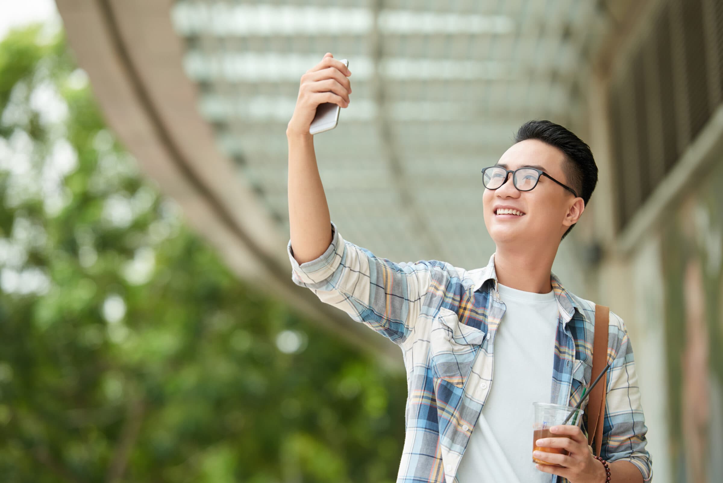A smiling student outdoors holding an iced drink and a phone